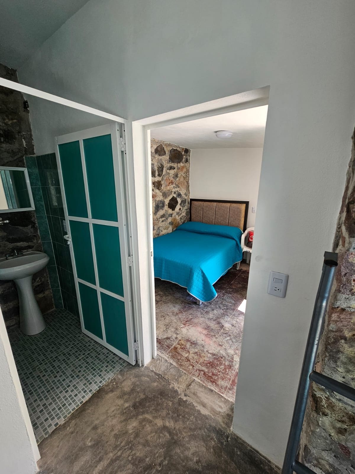 Un dormitorio con cama, pared de piedra y baño con lavamanos y espejo.