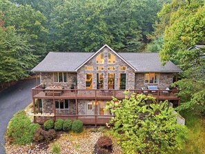 A two-story stone house with a balcony, surrounded by dense forest. - Charming 6-bedroom house in Wintergreen Resort with AC (Wintergreen Resort)