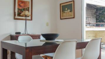 A dining area with a round table, white chairs, and two framed artworks on the walls.