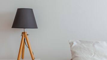 A room with a white bedside table, a lamp with a dark shade, and a bed with a white pillow.