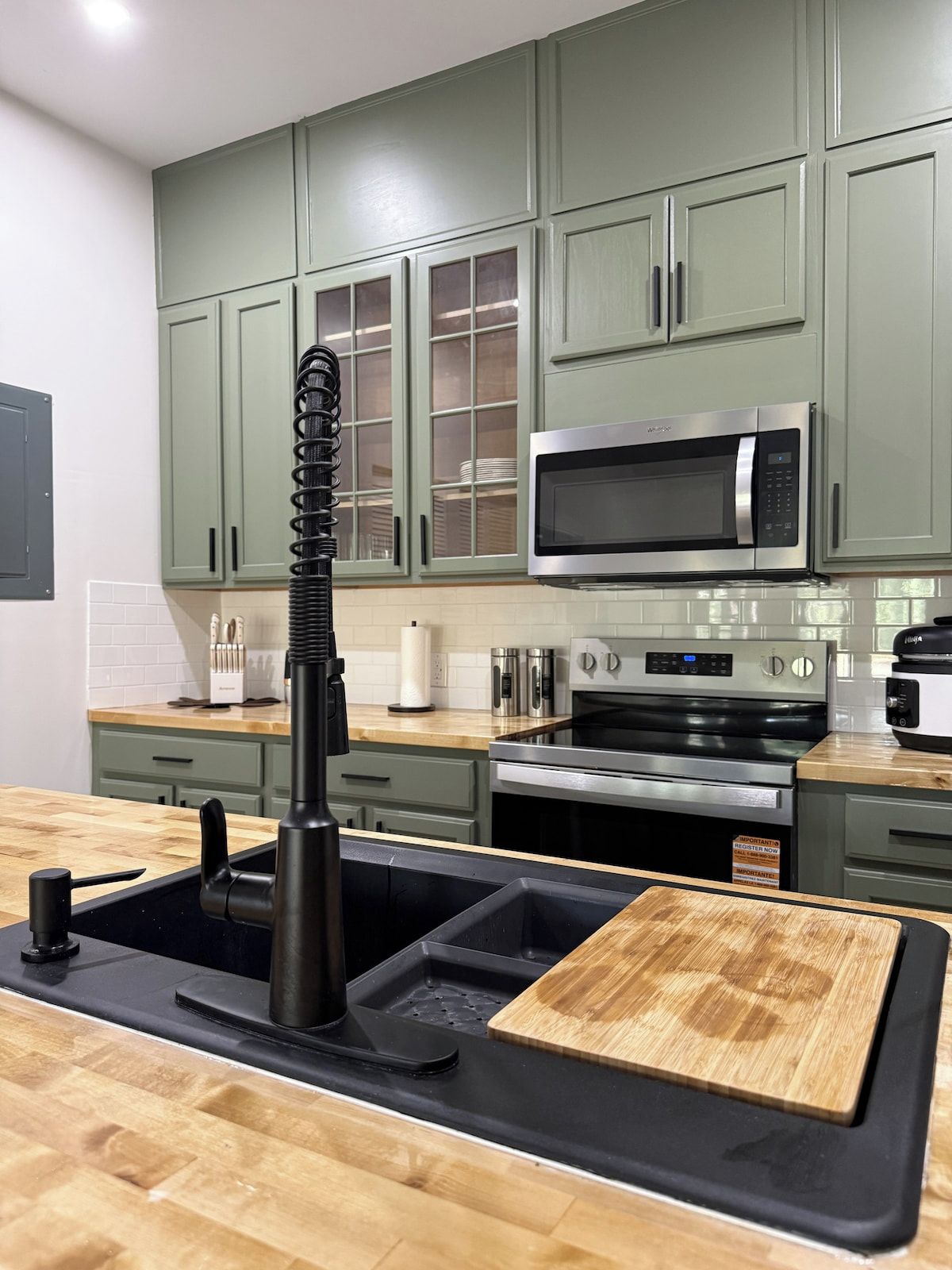 A kitchen with green cabinets, a stainless steel microwave, an oven, and a sink with a black faucet.