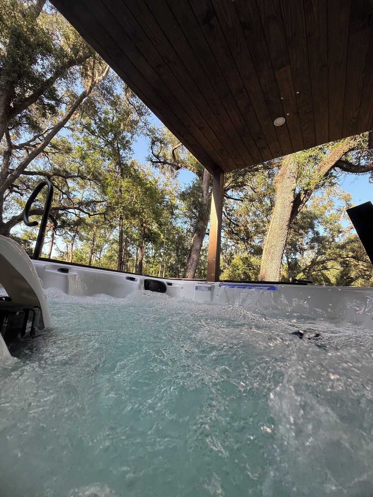 A hot tub under a wooden canopy surrounded by trees.