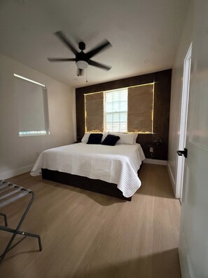 Une chambre à coucher avec un lit, un ventilateur de plafond, une fenêtre et une porte.