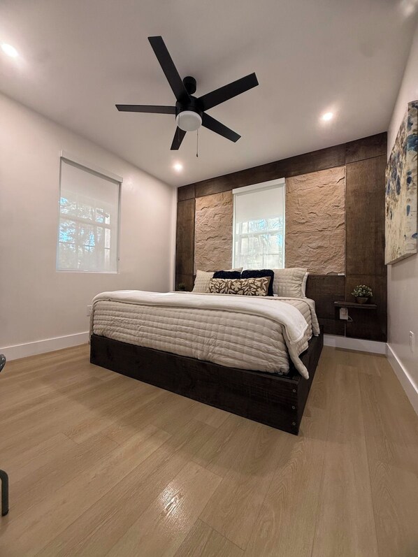 A bedroom with a bed, a ceiling fan, a window, and a wall-mounted shelf.