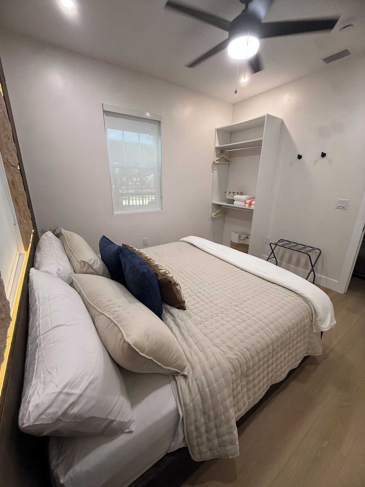 A bedroom with a bed, pillows, a ceiling fan, a window, and a wardrobe.