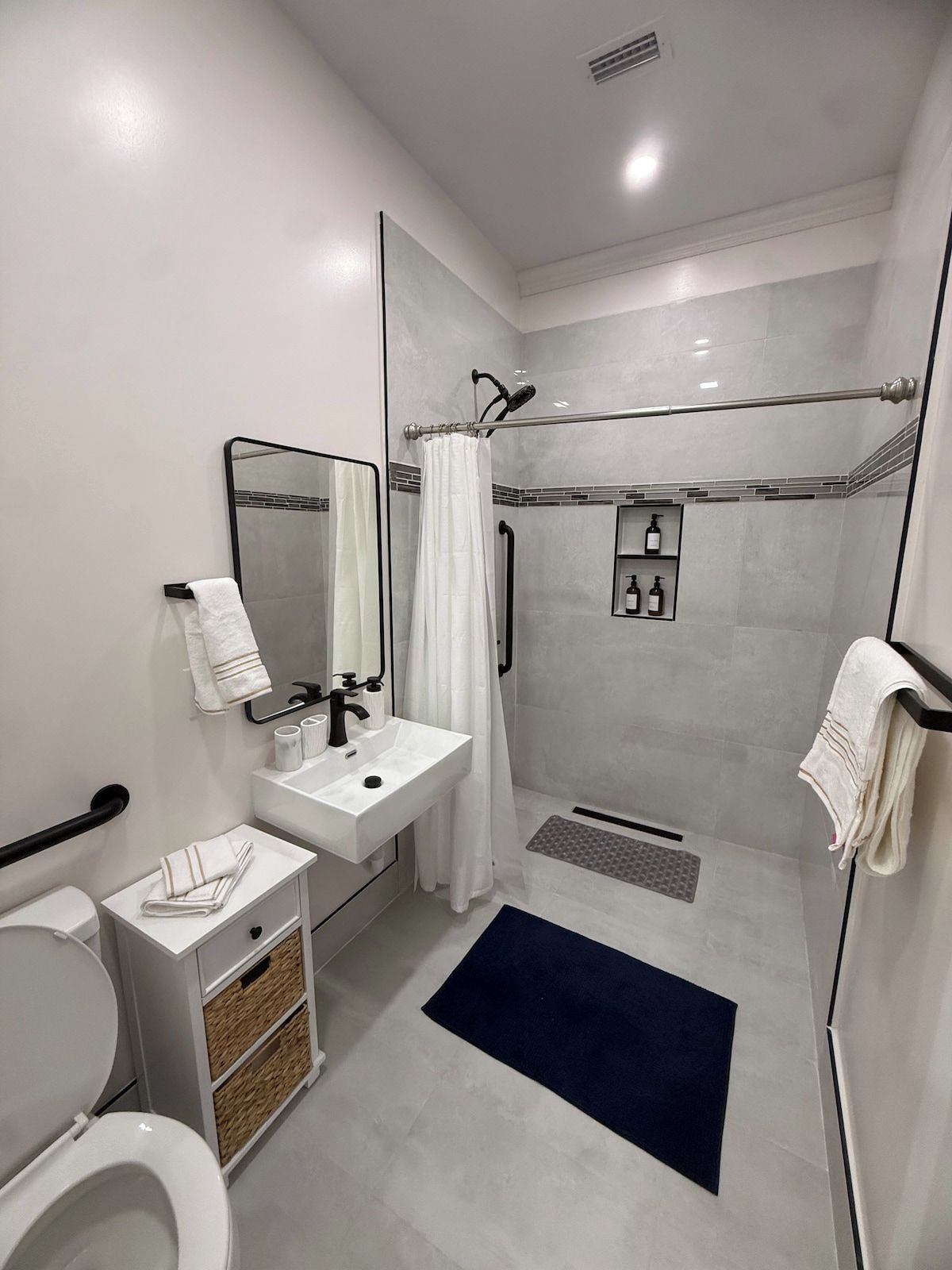 A modern bathroom with a toilet, sink, mirror, shower, and a towel rack.
