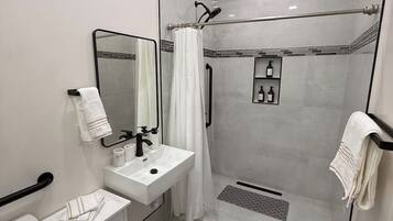 A modern bathroom with a toilet, sink, mirror, shower, and a towel rack.