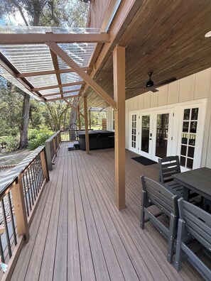 Une terrasse extérieure couverte, dotée d’un plancher en bois, d’un barbecue et d’un espace détente avec des chaises et une table.