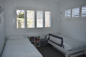 Ein Schlafzimmer mit zwei Einzelbetten, einem kleinen Bücherregal und einem Fenster mit Rollläden.