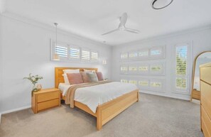 A bedroom with a bed, bedside tables, a ceiling fan, and windows with blinds. - Coastal Living at Its Best – Stunning Spacious 4-Bedroom Family Home (Port Macquarie)