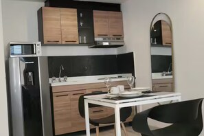 A compact kitchen with a microwave, refrigerator, and a dining table set for two. - New Listing (Bogotá)