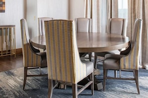 A round dining table with six chairs, each with a patterned backrest. The room has a carpeted floor and a window with curtains. - Glacier Canyon  Wilderness Waterpark Wisconsin Dells, 2 BR 1,500 sq ft Condo (Baraboo)