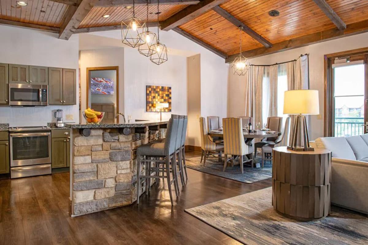 A spacious kitchen with a stone island, wooden ceiling beams, and modern lighting fixtures.