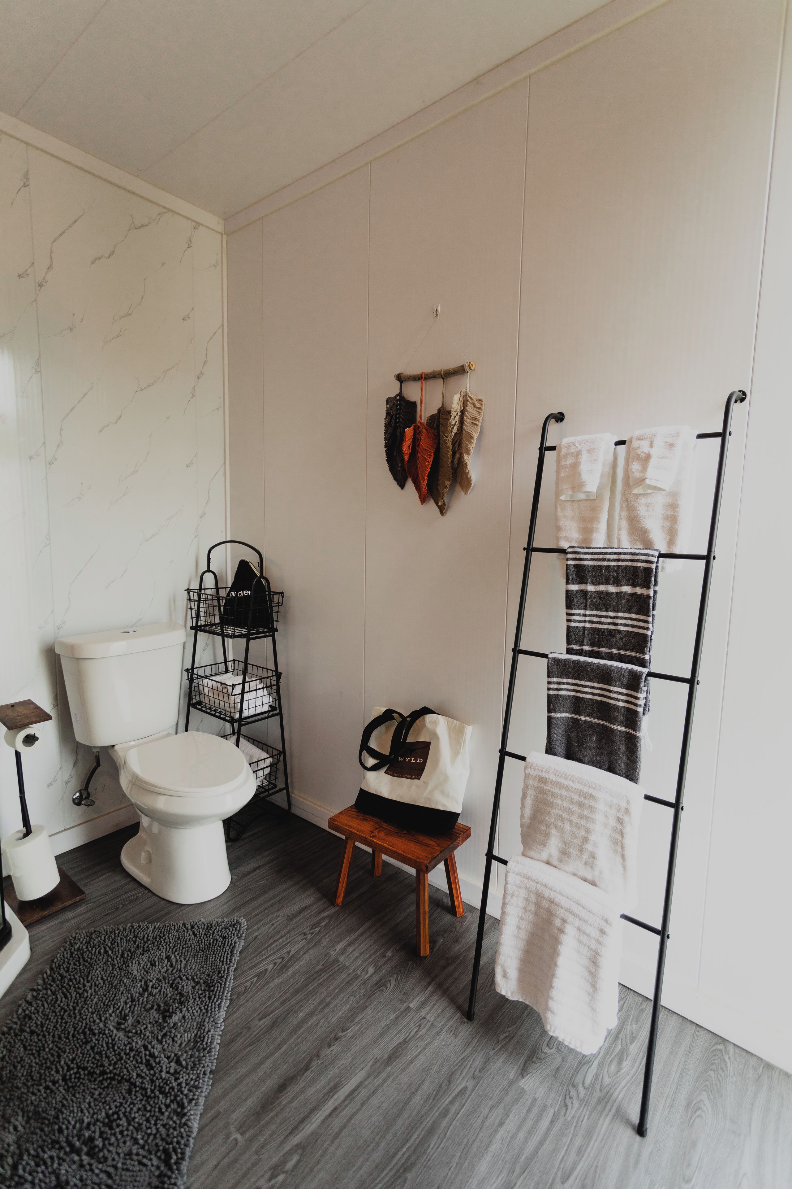 Un baño con inodoro, toallero, repisa con bolsas y un taburete pequeño.
