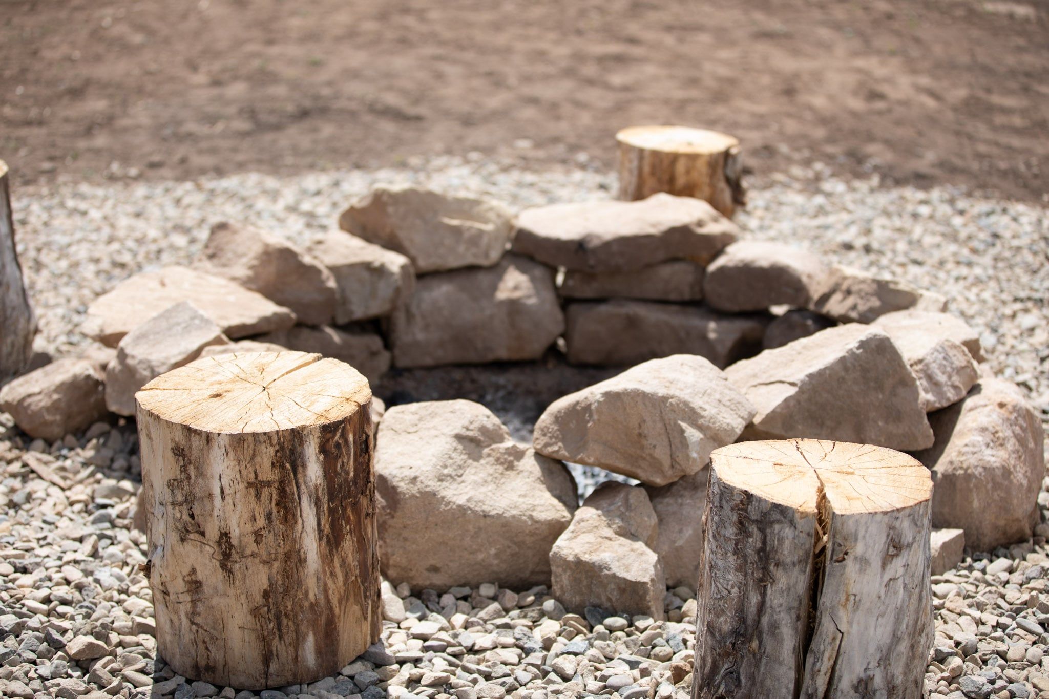 A pile of large rocks and tree stumps arranged in a circle on a gravel surface.