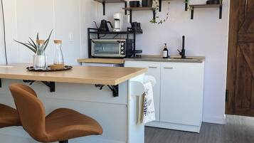 A modern kitchen with a central island, bar stools, a microwave, a coffee maker, and hanging plants.