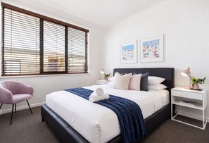 Een moderne slaapkamer met een groot bed, een nachtkastje, een stoel en een raam met zonwering.