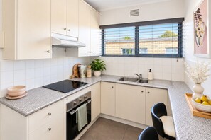 A kitchen with white cabinets, a black stove, a sink, and a window with blinds. - Sunlit South Yarra 2BR Apartment | Free Parking (South Yarra)