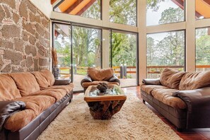 A spacious living area with leather sofas, a glass coffee table, and a stone wall. - Forest cabin for groups · hot tub and fire pits (Tres Marias)