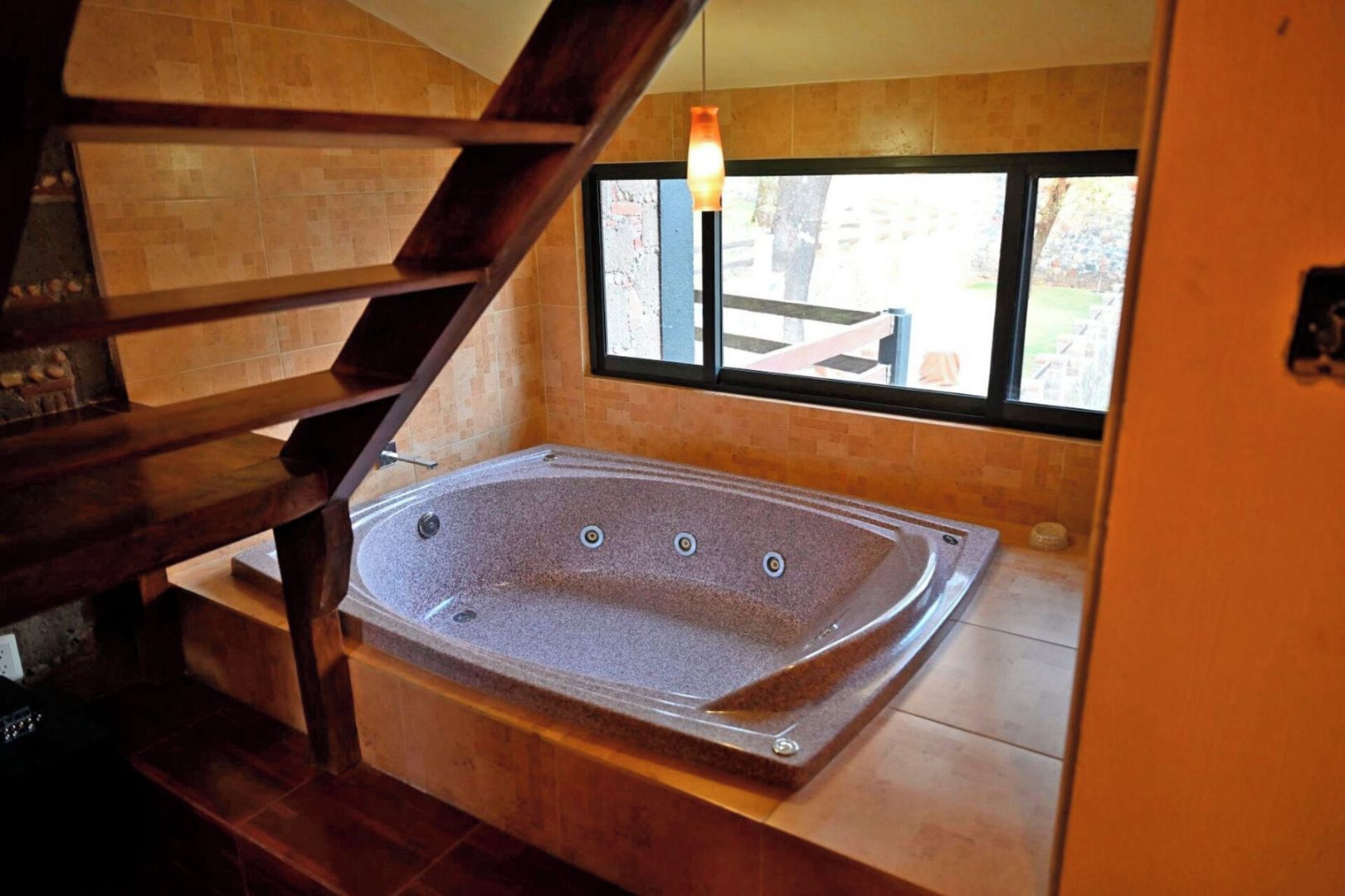 A spa area with a large freestanding bathtub, a wooden staircase, and a window with a view of the outdoors.