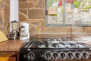 A kitchen with a gas stove, a coffee maker, and a stone wall. - Forest cabin for groups · hot tub and fire pits (Tres Marias)