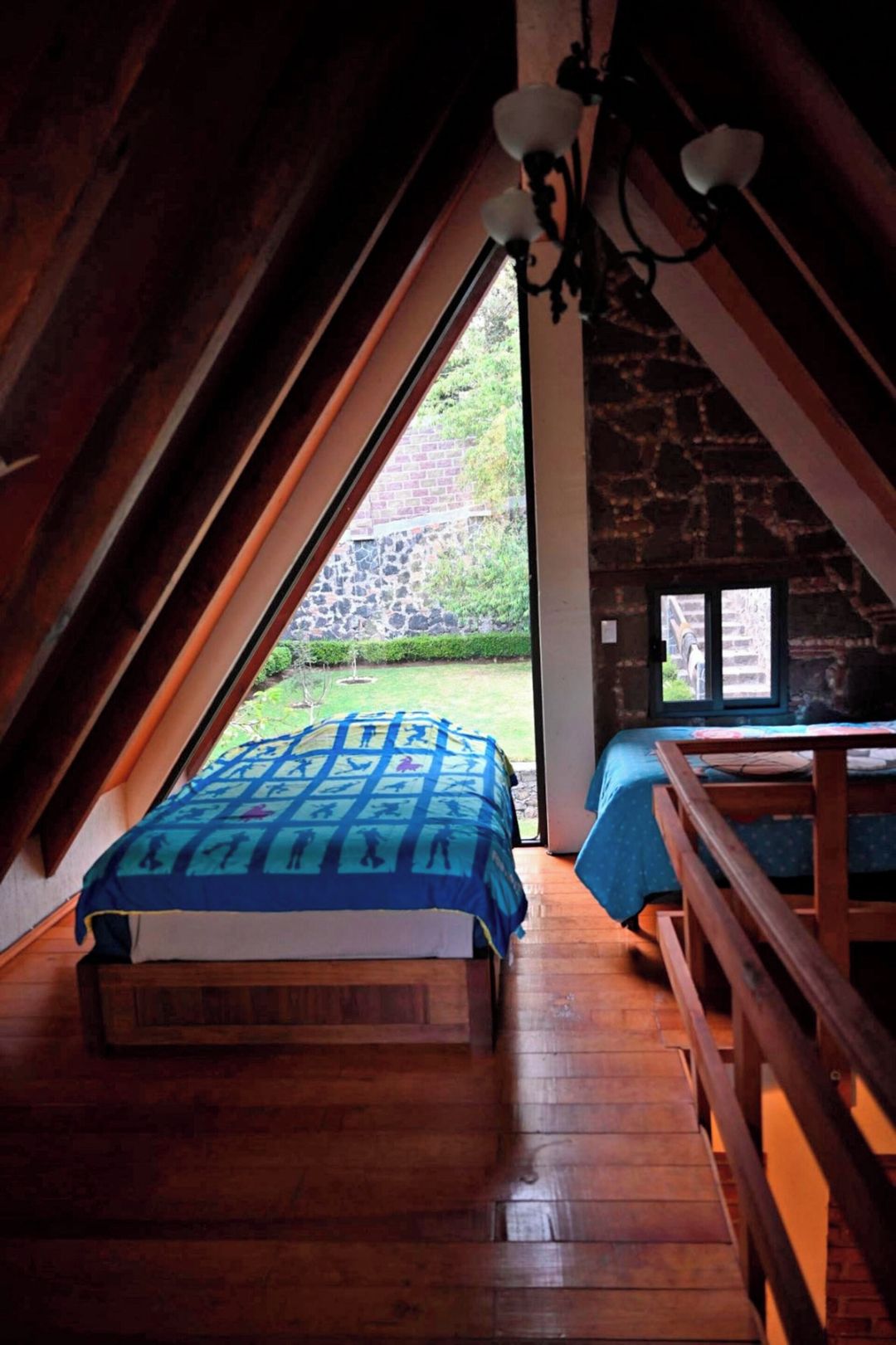 A bedroom with a wooden bed, a view of a garden through a window, and a stone wall.