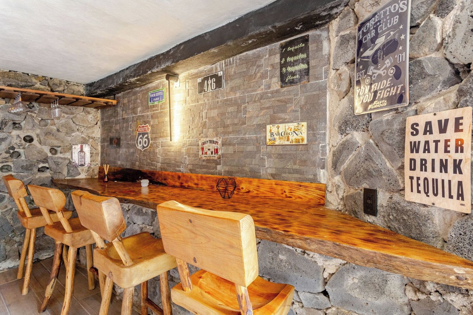 Uma área de bar com cadeiras de madeira e uma parede de pedra.