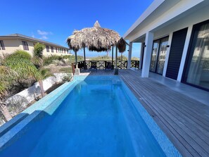 A swimming pool with a thatched roof structure, wooden deck, and a view of the ocean. - New Listing (Jan Thiel)