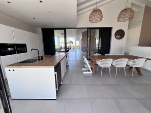 A modern kitchen with a central island, white cabinetry, and a dining area with white chairs. - New Listing (Jan Thiel)