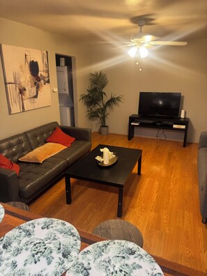 A living room with a leather sofa, a coffee table with a candle, a television on a stand, and a potted plant. - Cozy 1-bedroom apartment in delightful Houston with AC in the Midtown Area (Houston)