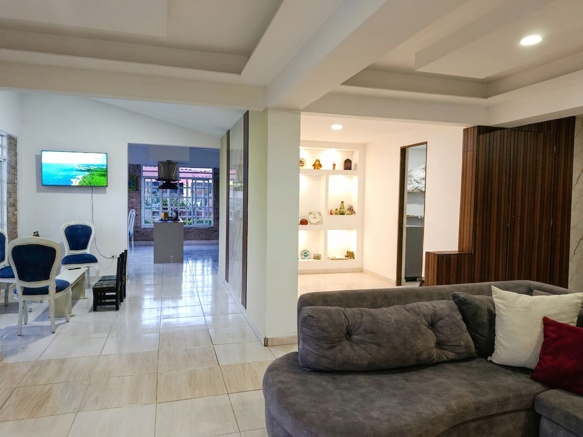 A modern living room with a grey sofa, a TV mounted on the wall, and a dining area with chairs and a table.
