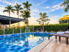 A swimming pool with a tiled deck, surrounded by palm trees and a covered seating area. - New Listing (La Tebaida)