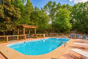 Une piscine entourée d’arbres, dotée d’une terrasse en bois et de chaises longues.