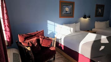 Hotellihuone, jossa on sänky, tuoli, yöpöytä ja seinään kiinnitetty lamppu.