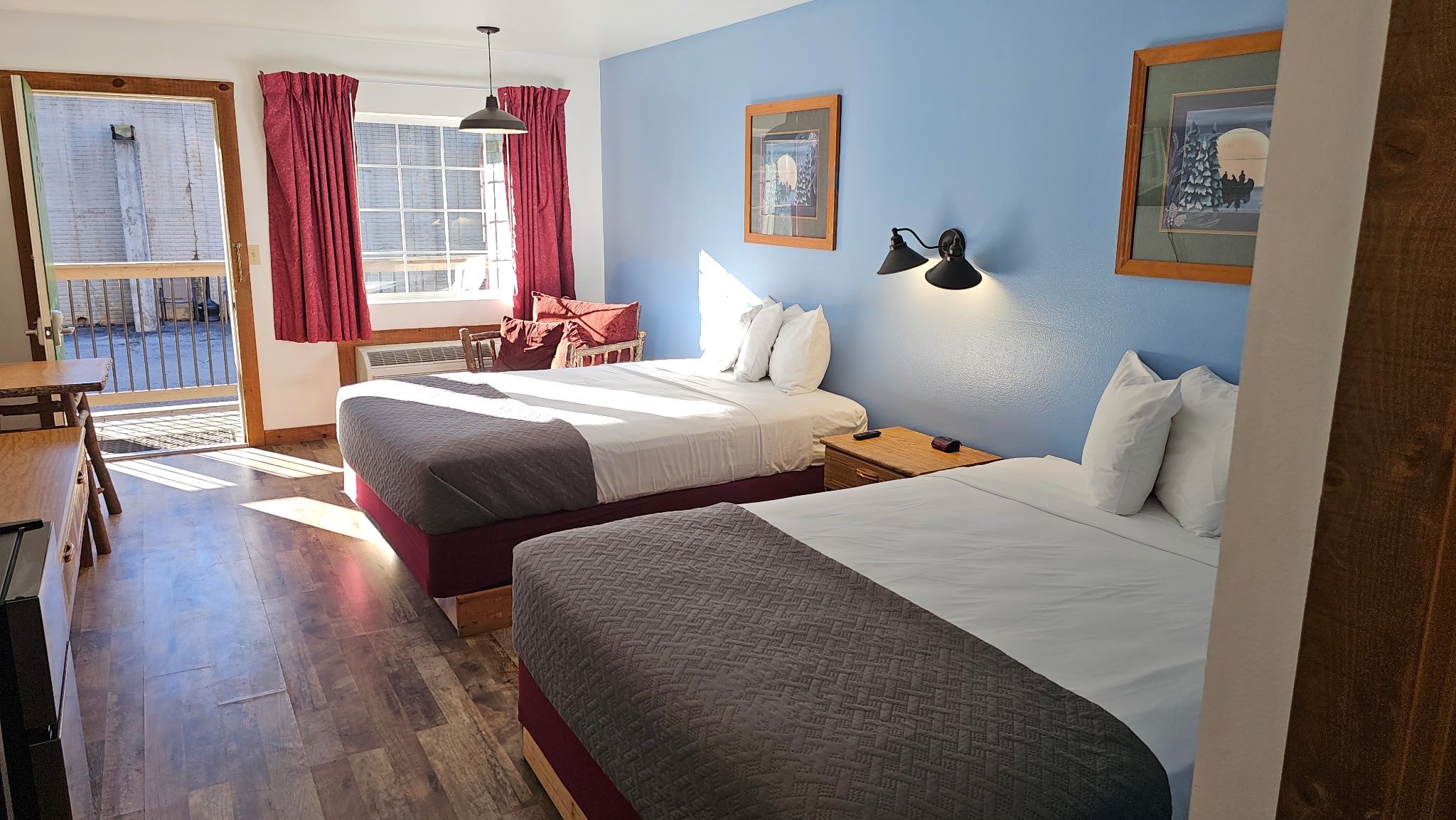 A hotel room with two beds, a dining table, and a view of the outside.