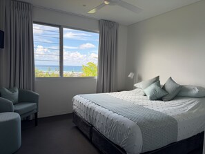 Ein Schlafzimmer mit einem Bett, einem Sessel, einem Fenster mit Vorhängen und einem Deckenventilator.