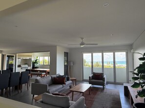 Ein modernes Wohnzimmer mit einer Couch, Sesseln, einem Couchtisch und Meerblick durch große Fenster.
