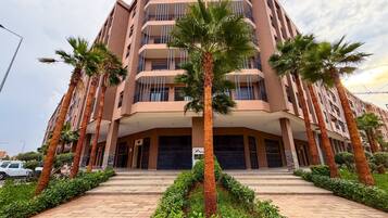 A multi-story building with a central entrance, surrounded by palm trees and a paved walkway.