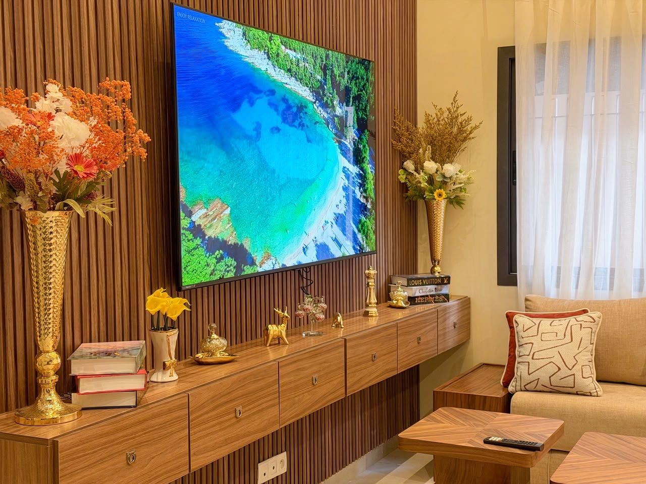 Una sala de estar con una televisión de pantalla plana montada en una pared de madera, un sofá, una mesa de centro y una mesita auxiliar con adornos.