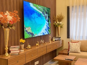 Una sala de estar con una televisión de pantalla plana montada en una pared de madera, un sofá, una mesa de centro y una mesita auxiliar con adornos.