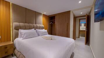 A modern bedroom with a large bed, wooden paneling, a bedside table, and a TV mounted on the wall.