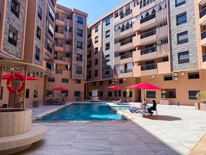 Un edificio residencial de varios pisos con piscina, mobiliario exterior y balcones.