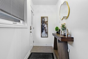 A hallway with a door, a framed abstract painting, a mirror, and a console table with decorative items. - The extravagant minimalist 3 (Gatineau)