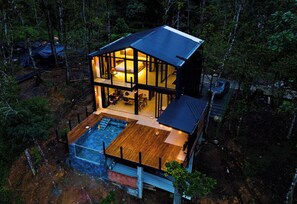 A two-story modern house with a large glass facade, a swimming pool, and a deck area. - Kilamo Sky: Sleep Under the Stars, Wake Up in Paradise - Macas Ecuador (Macas)