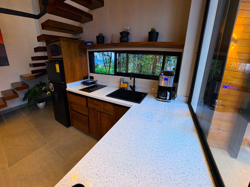 A modern kitchen with a white countertop, built-in appliances, and a window with a view of trees.