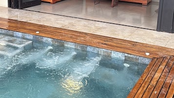 A modern outdoor seating area with a pool, wooden deck, and a flat-screen TV mounted on the wall.