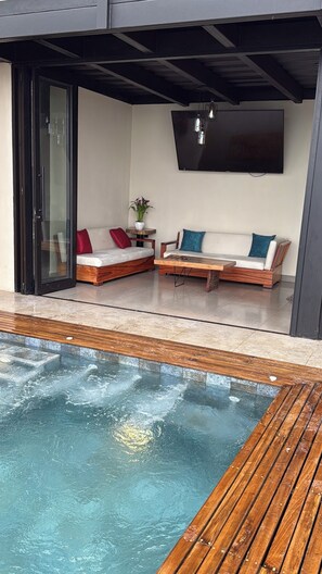A modern outdoor seating area with a pool, wooden deck, and a flat-screen TV mounted on the wall. - Kilamo Sky: Sleep Under the Stars, Wake Up in Paradise - Macas Ecuador (Macas)