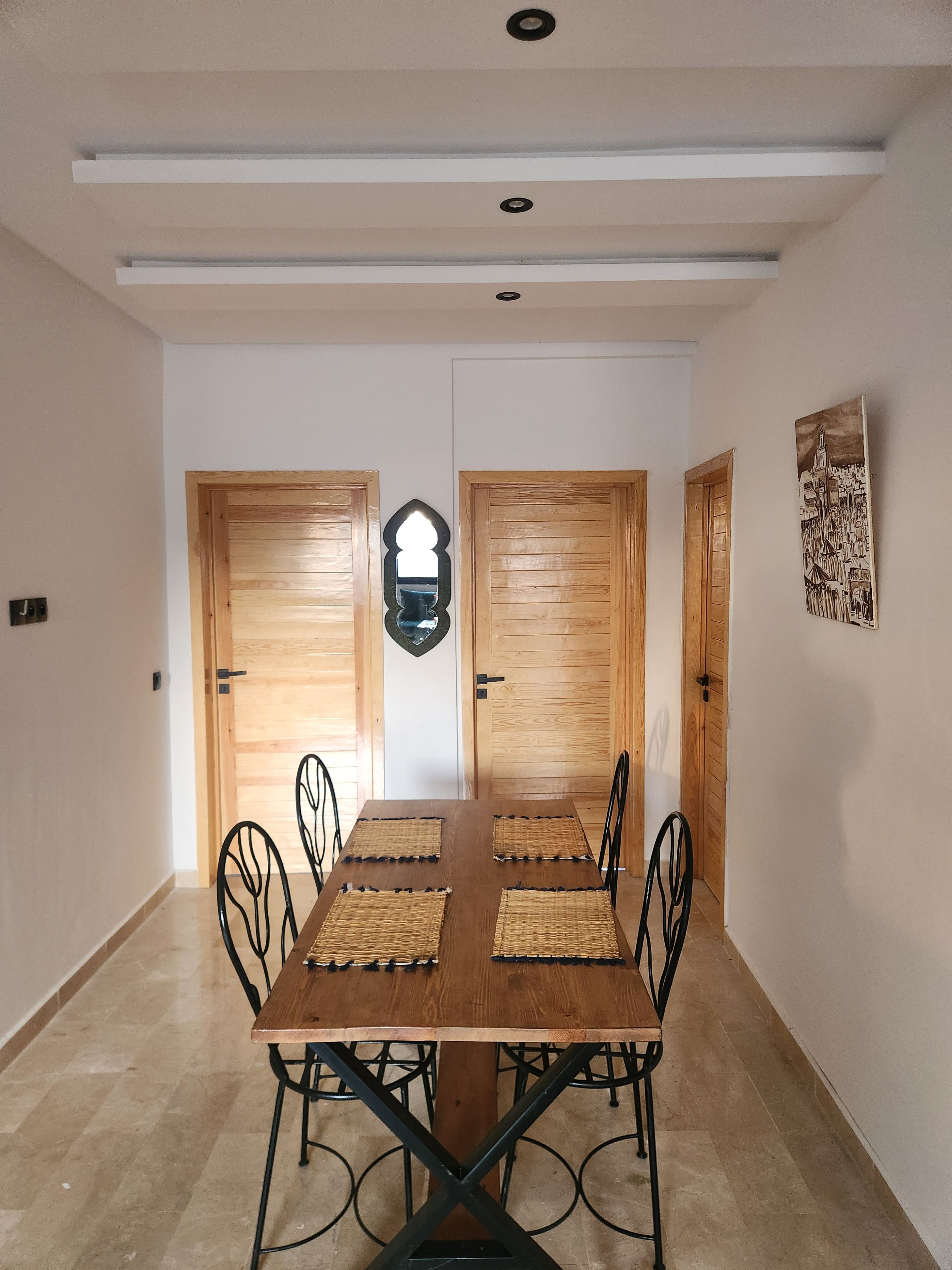 A dining area with a wooden table, four chairs, and a decorative mirror on the wall.