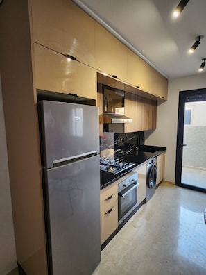 Una cocina moderna con un refrigerador de acero inoxidable, estufa a gas, horno empotrado y lavadora.