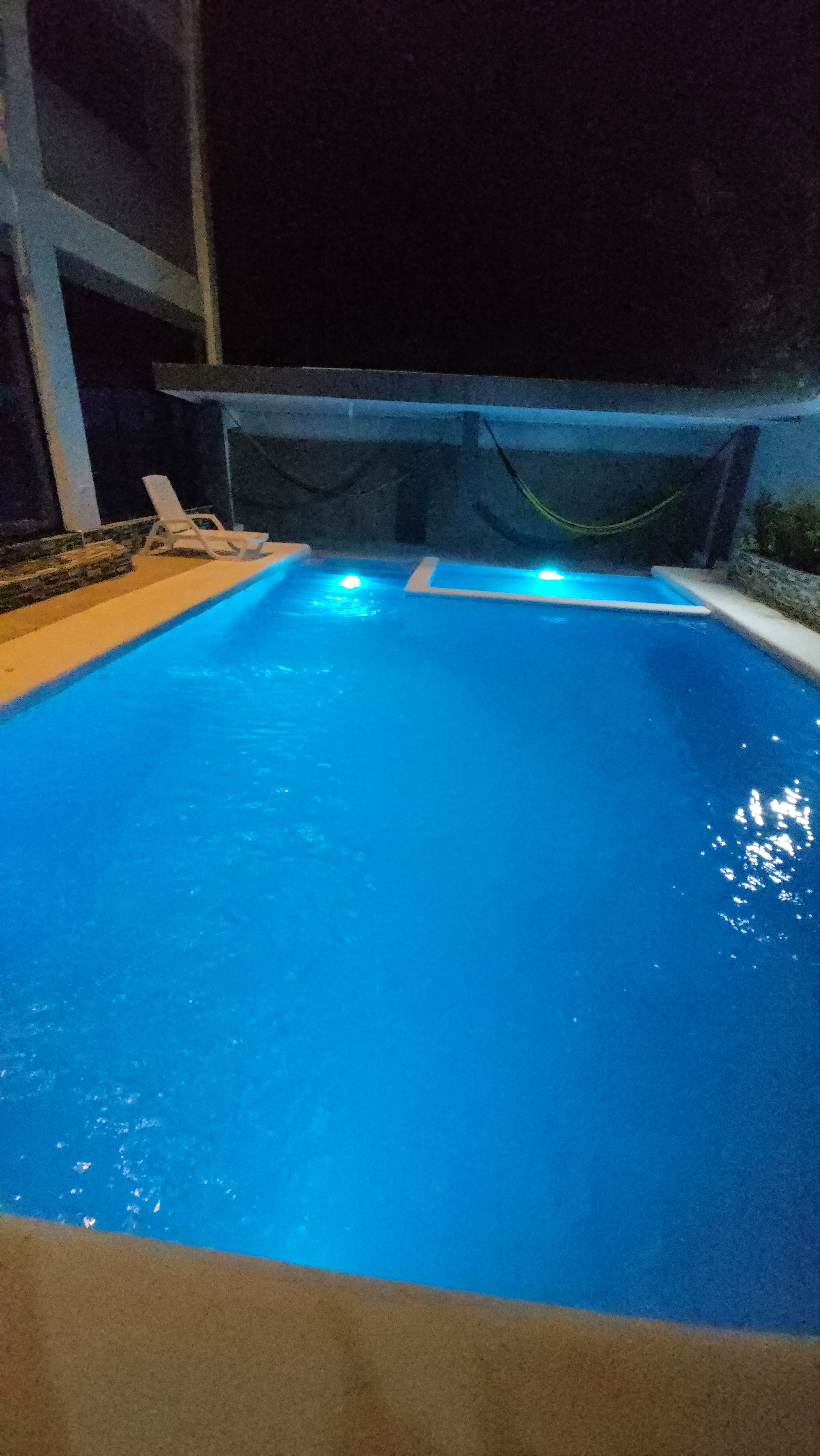 Una piscina con bordo piastrellato e una poltrona da relax bianca.